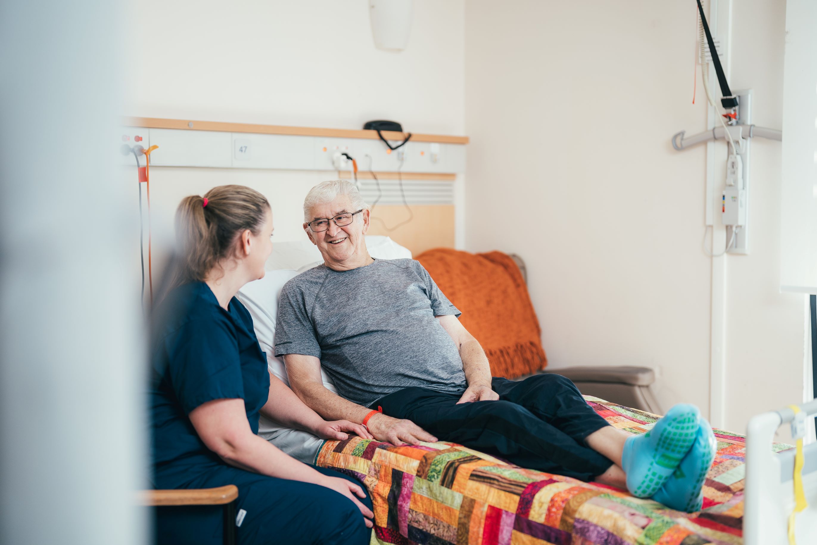 A doctor sits in a chair smiling and talking to an older woman