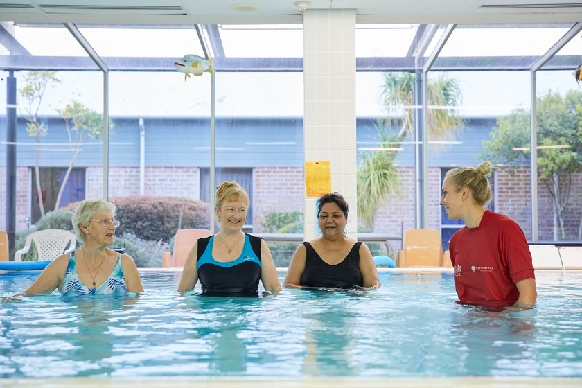 St John of God allied health professional instructs three patients waist deep in pool
