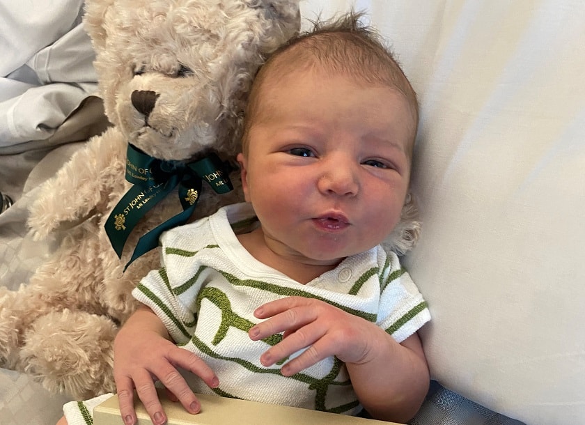 Newborn baby wearing striped onesie laying next to teddy bear