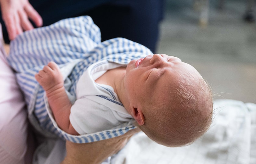 A newborn baby boy swaddled in a cloth being held.