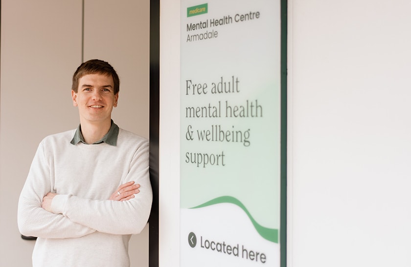 Medicare Mental Health Centre's Liam Dekker, Service Manager South, standing in front of a MMHC sign.