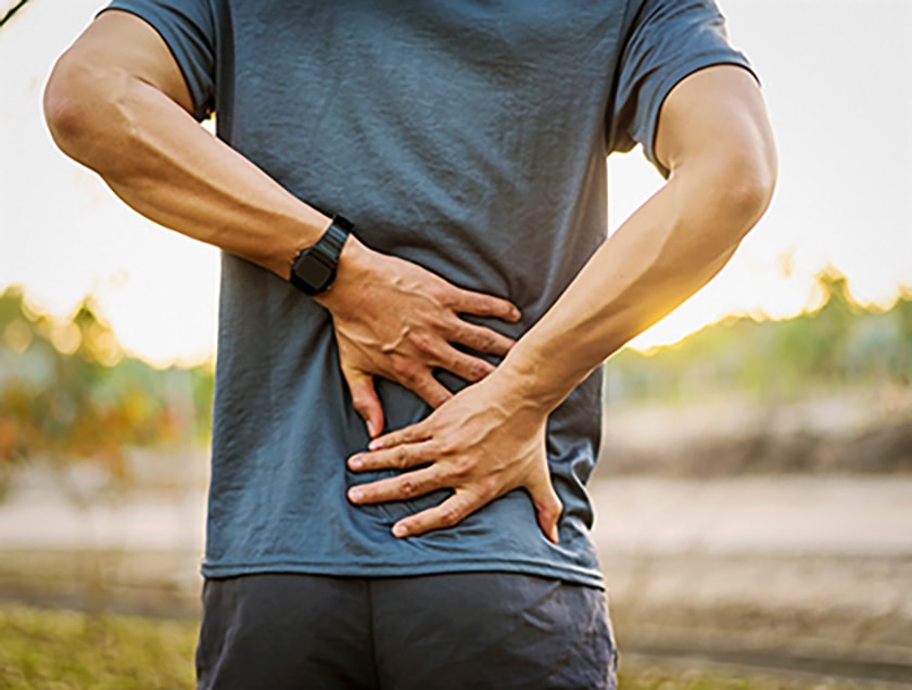 Person wearing activewear and a smart watch holding lower back area from the perspective of behind