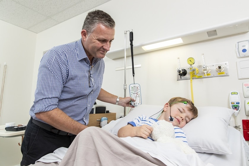 Doctor checking on paediatric patient lying in bed during a sleep study