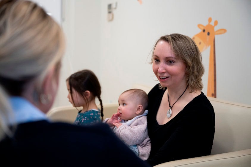 A woman sits talking to a caregiver with her baby on her lap.