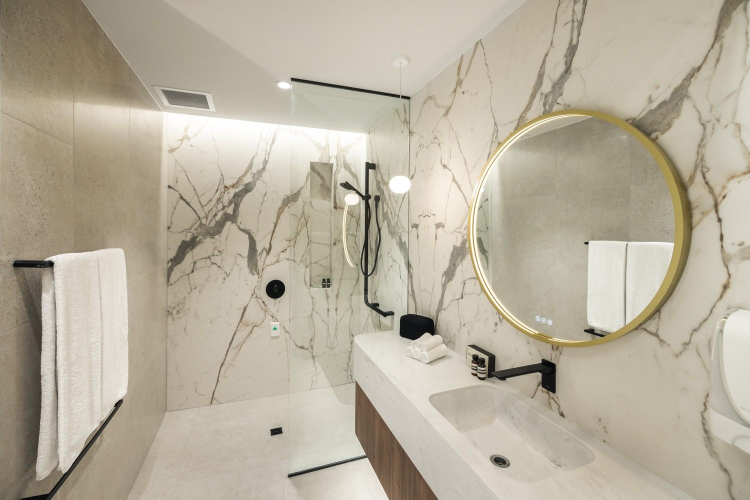 The bathroom in The Suites with white marble-style tiles on the walls