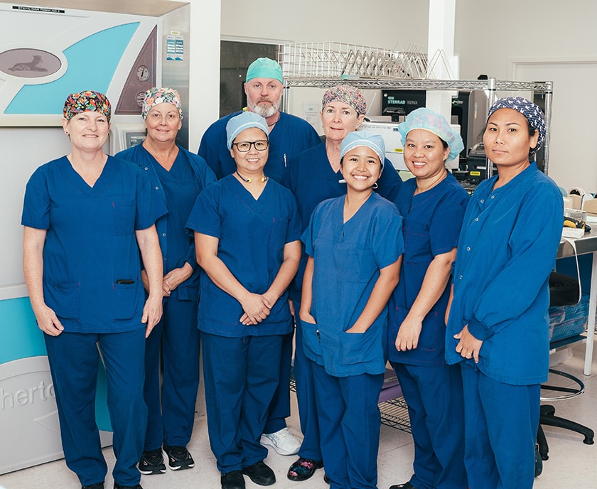 A group of caregivers wearing scrubs smile for a photo