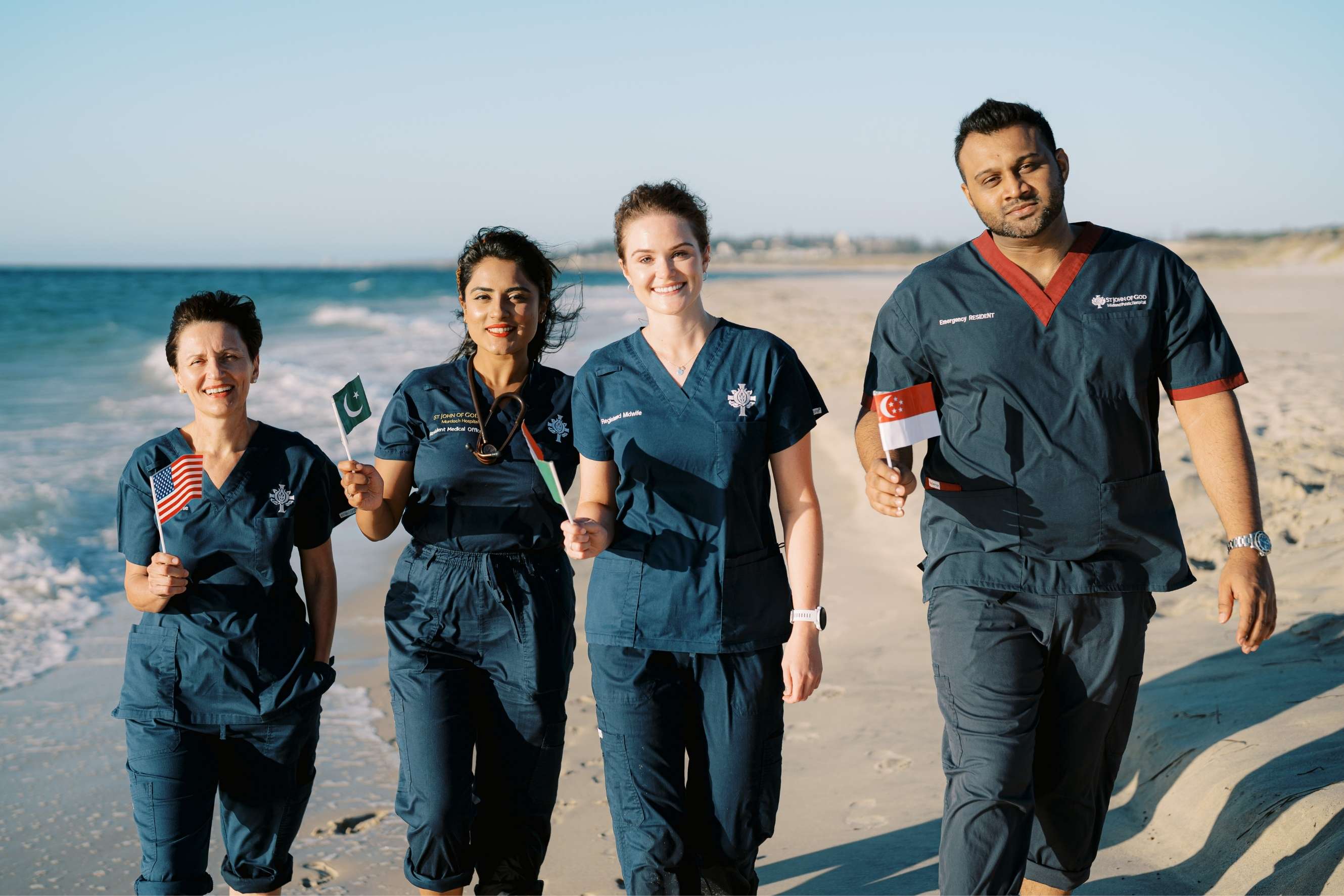 4 healthcare professionals walking on the beach while holding flags from their countries