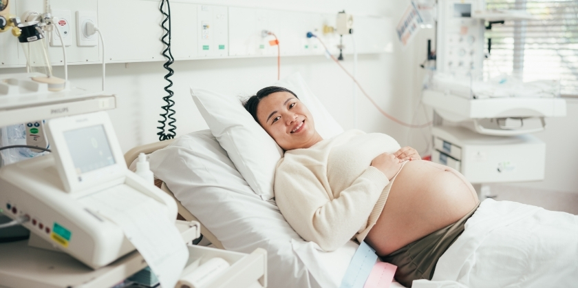 A pregnant woman lying in a hospital bed, smiling at the camera