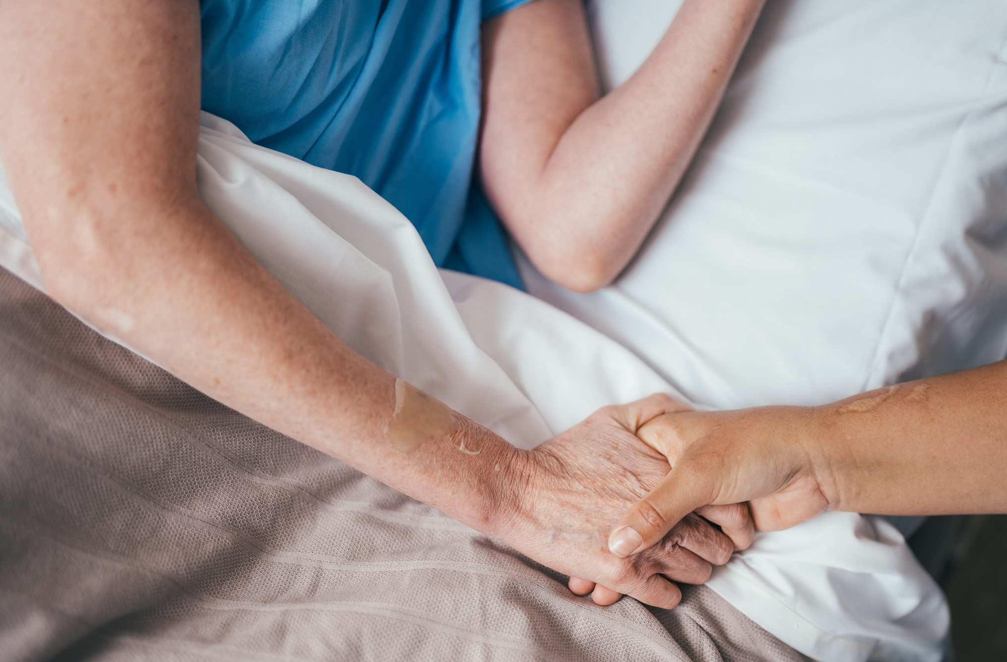 Hands from 2 different people holding each other in a caring way on a hospital bed