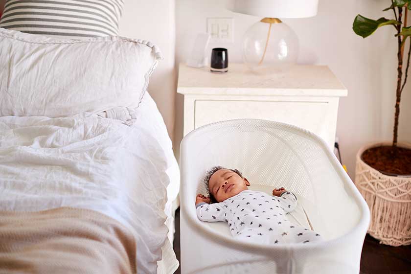 Newborn baby asleep in bassinet next to bed
