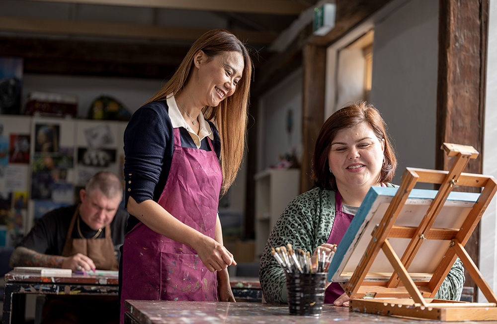 A client shows a caregiver her painting during an art day program