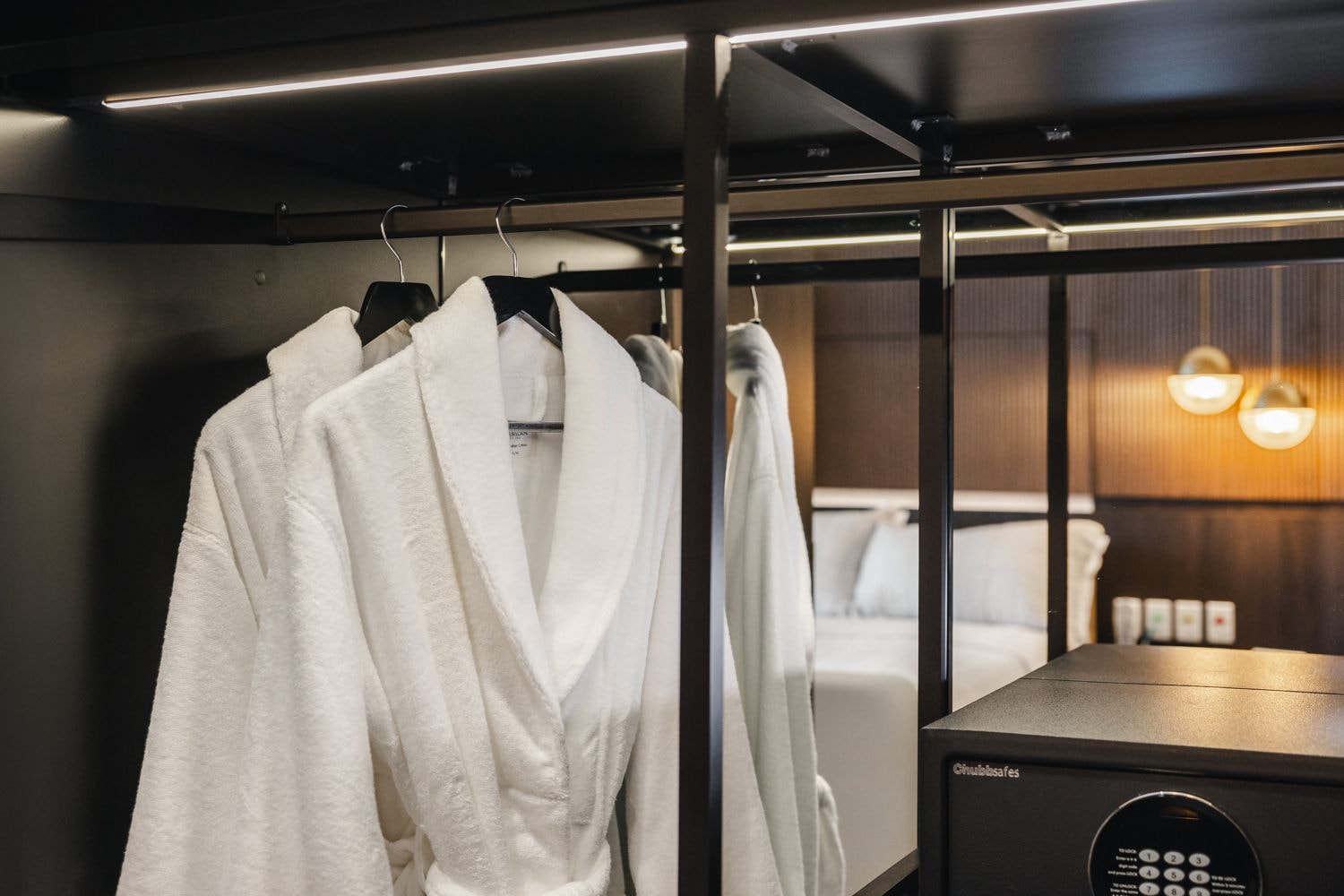 A couple of white robes hanging in the wardrobe in The Suites