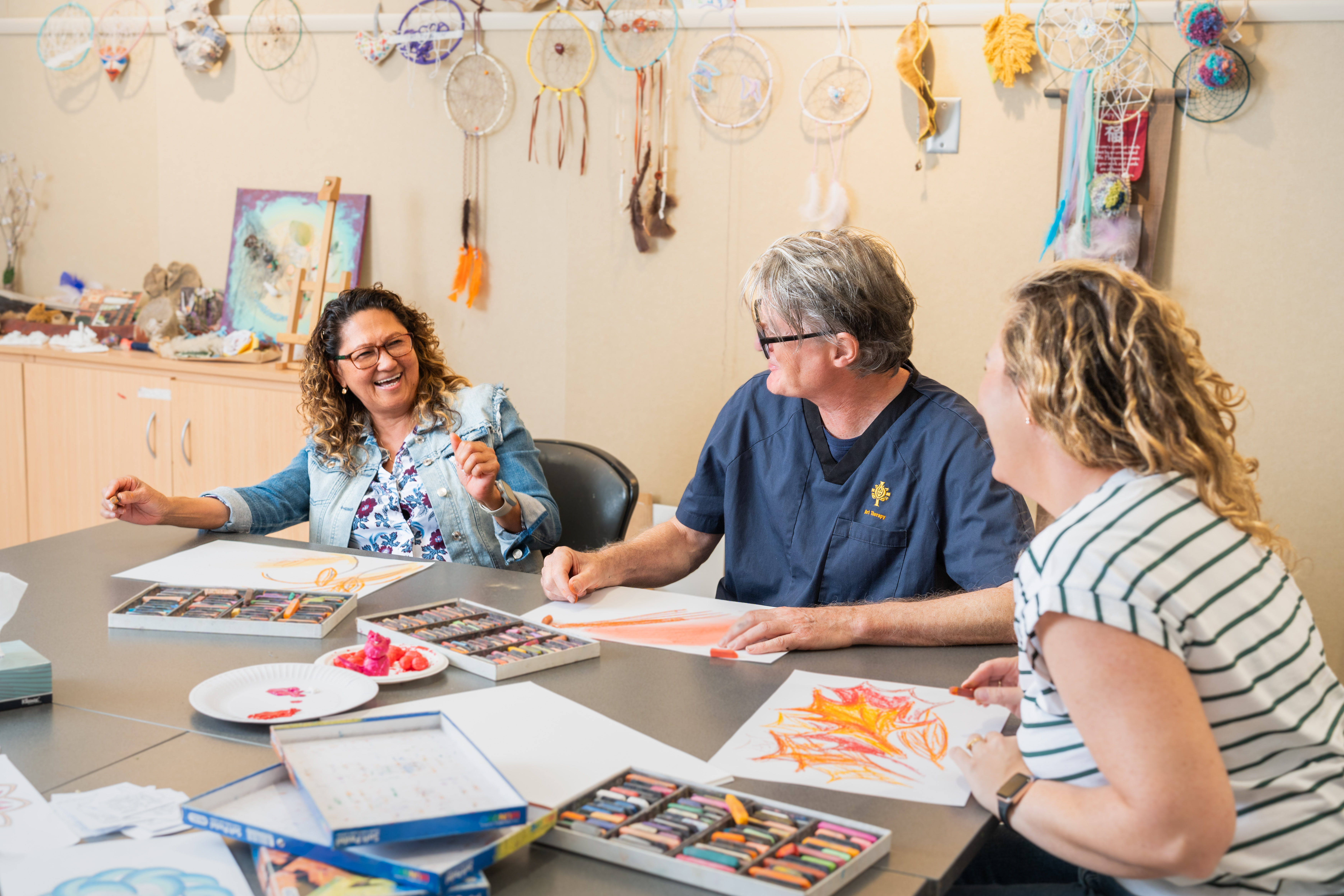 Three people sit around a table while talking to each other and making art