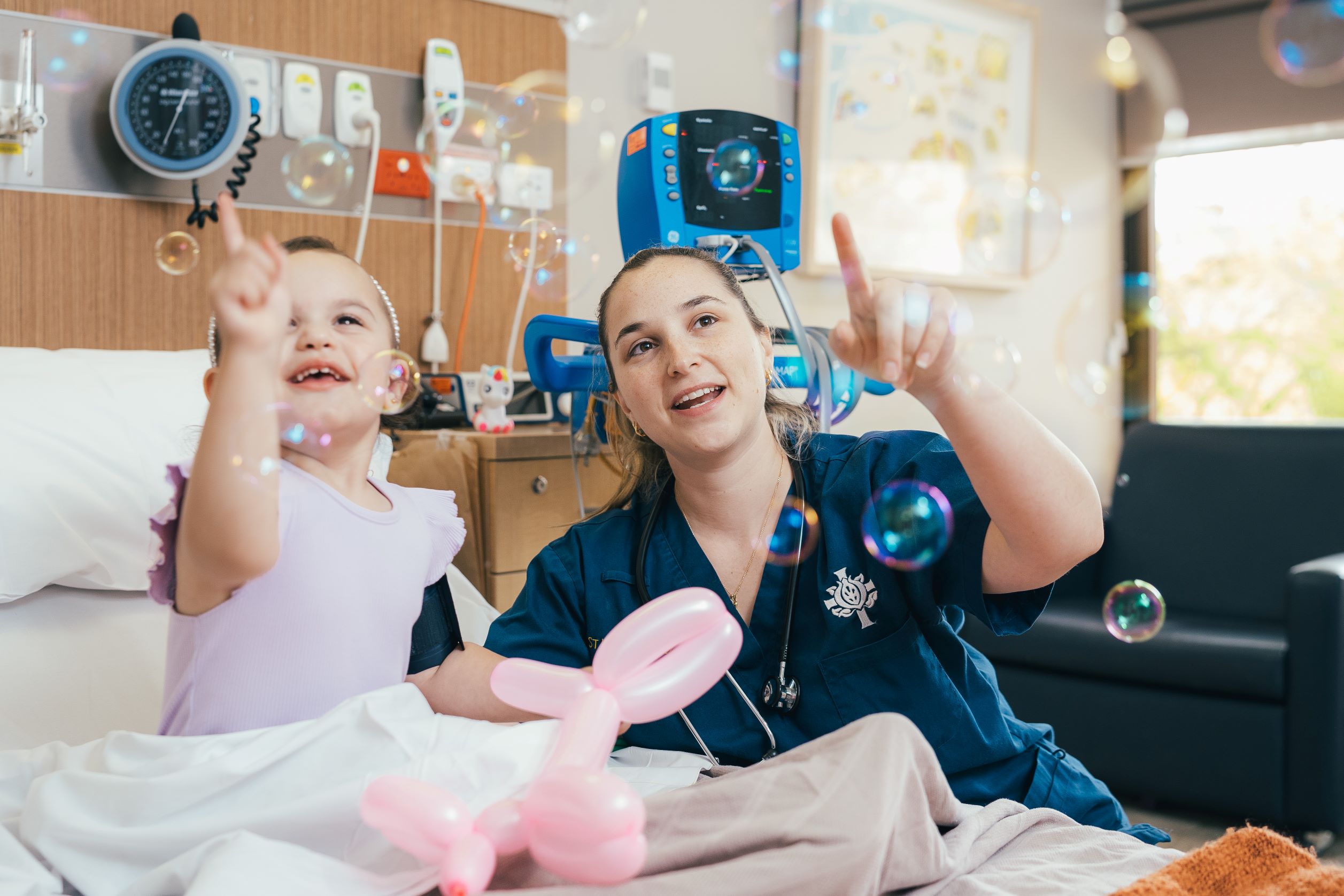 A health professional and a toddler are playing with soap bells in a hospital room