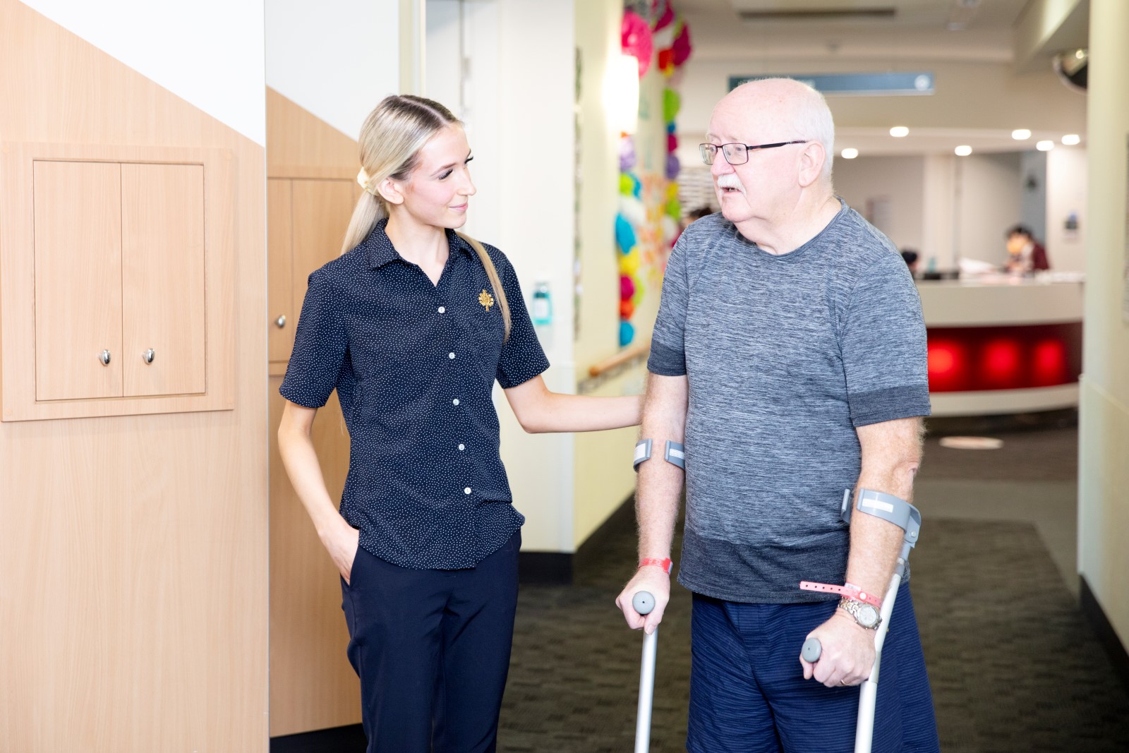 An elderly man on crutches speaking to a health professional in a hospital hallway