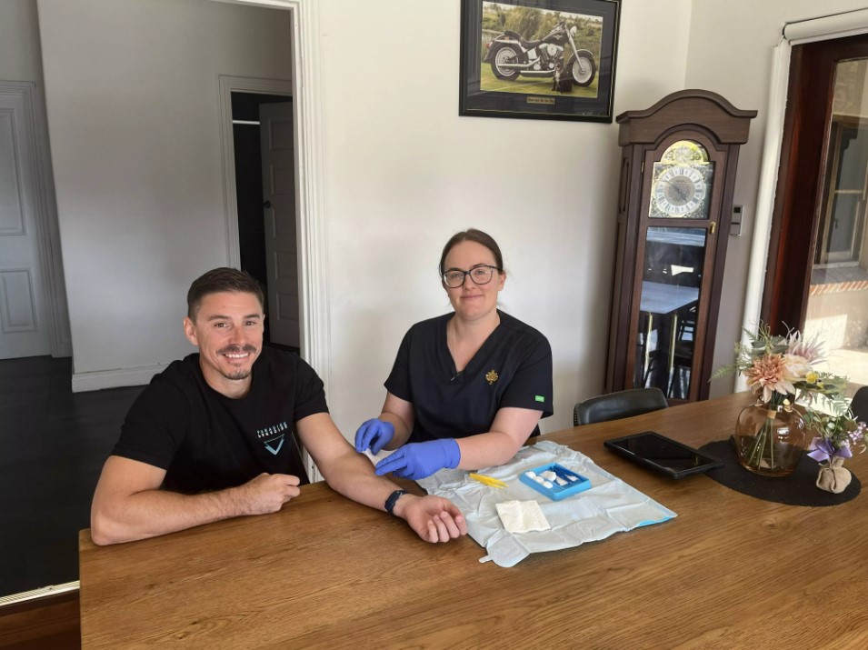 A healthprofessional draws blood from a patient at their home on the dining table 