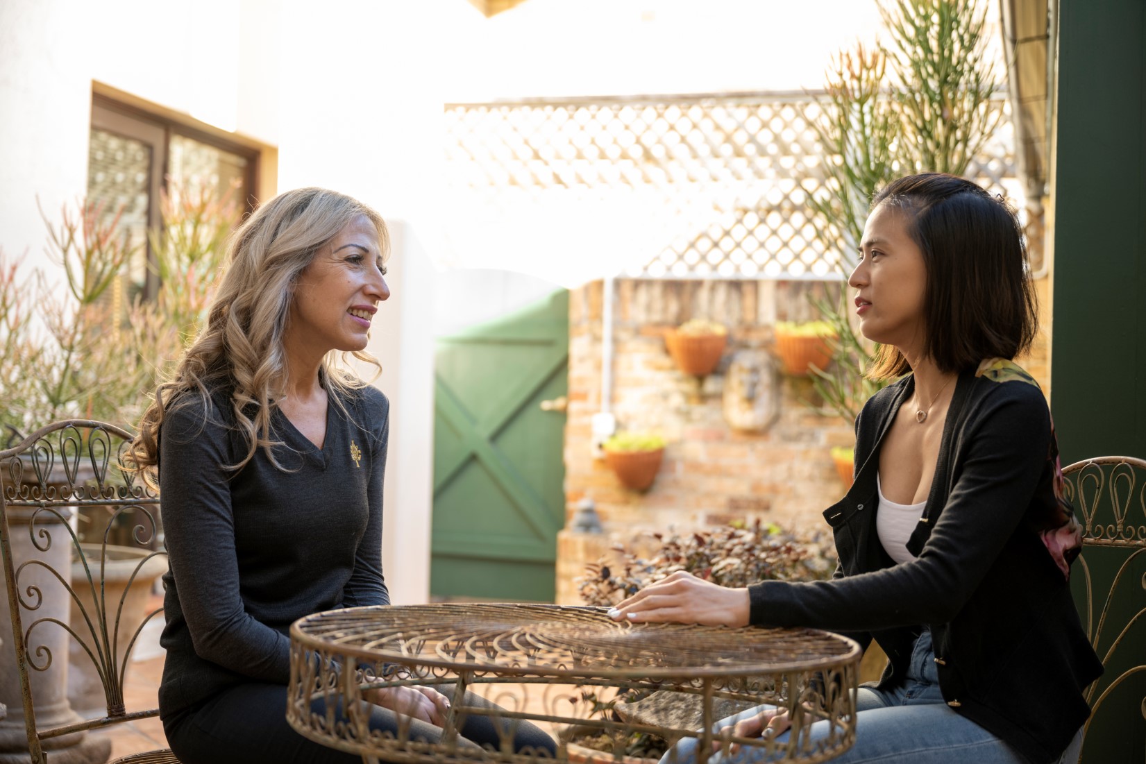 Two woman having a conversation over a table in a sunny patio