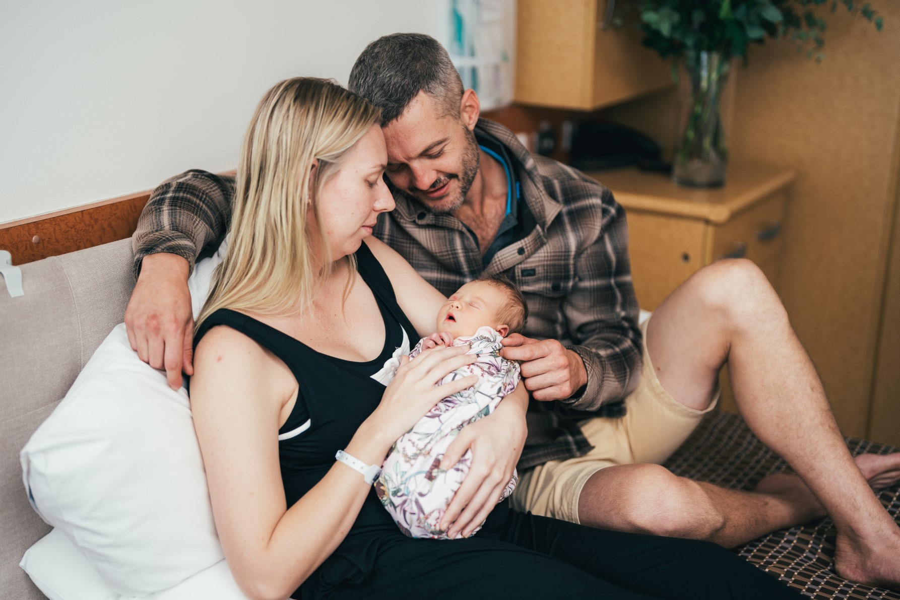 two proud parents with a newborn in mother's arms are resting on a bed