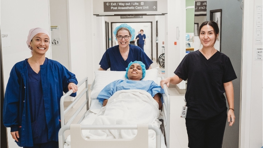 Surgical caregivers wheeling a patient in bed to theatre