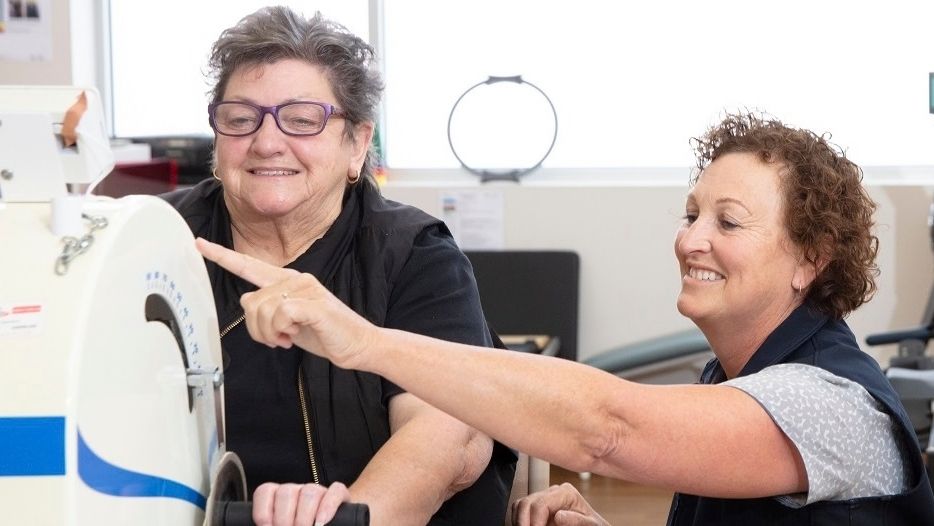 A caregiver helps a person on a rehab machine
