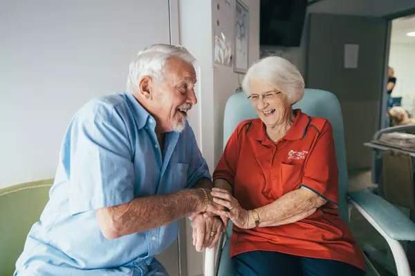 An elderly couple sits happily in the hospital while laughing together