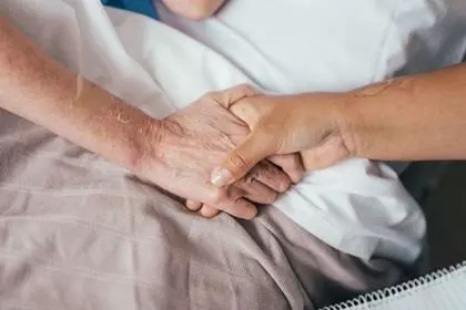 a younger and older hand are holding each other on the side of a bed